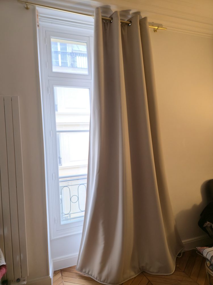 Rideau lourd beige devant une haute fenêtre dans un appartement ancien