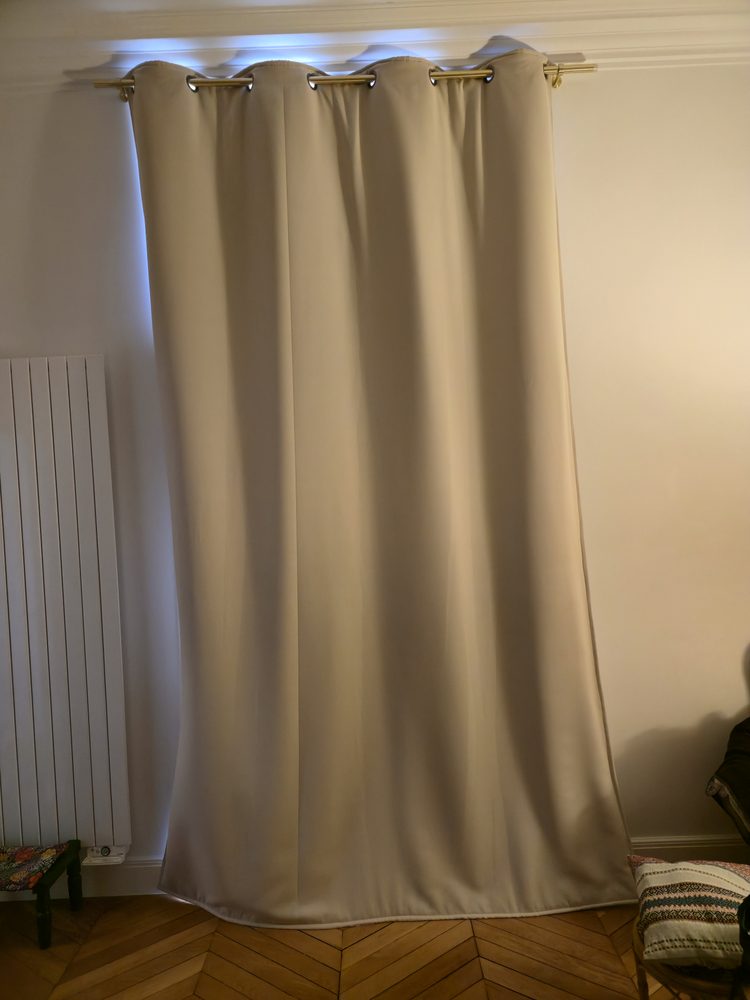 Rideau lourd beige tiré devant une fenêtre au-dessus d’un radiateur